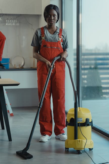 Three professional cleaners from End of Tenancy House Cleaning stand in a modern living room during a comprehensive domestic cleaning session. The room features a light-colored tiled floor, which is b